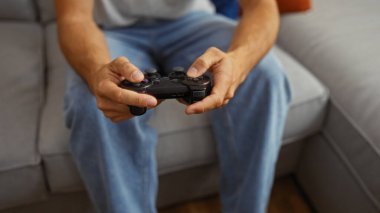Oturma odasında kanepede oturan genç bir adam video oyunları oynuyor, elinde bir kumanda, evde rahat bir ortam yaratıyor..