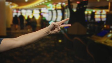 Canlı bir kumarhanede kumar makineleriyle barış işareti gösteren, neşeli bir atmosfer yakalayan ve oyun ortamında şans ve boş zamanı ima eden bir adam..