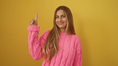 Pembe süveter giymiş, parlak sarı arka plana doğru gülümseyen genç güzelliği ve neşeli ifadeyi vurgulayan bir kadın.