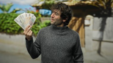 Bir şehir caddesinde elinde Czech Koruna banknotları olan İspanyol bir adam, kentsel bir ortamda finansal kazanç ve kültürel çeşitliliği vurguluyor..