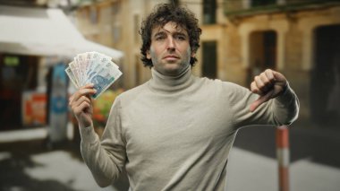 Polonya 'da bir şehir caddesinde İspanyol bir adam düşünceli bir ifadeyle zloty banknotlar sergiliyor ve şehir ortamında baş parmak işareti yapıyor..