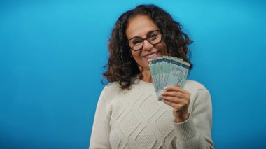 Orta yaşlı bir kadın elinde mavi izole arka plan duvarına karşı Malezya halka banknotları tutarak gülümsüyor..