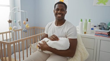 Yakışıklı genç adam yatak odasında oturmuş beşiği beyaz battaniyeye sarmış, camdan içeri ışık sızıyor..