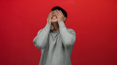 İzole edilmiş kırmızı arka plan duvarına karşı elleri başının üstünde duygularını ifade eden genç bir adam..