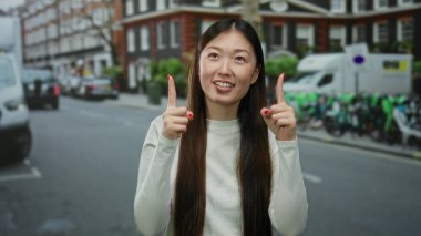 Uzun saçlı, gülümseyen ve arka planda arabaları ve bisikletleri olan açık havada beyaz gömlek giyen bir kadın..