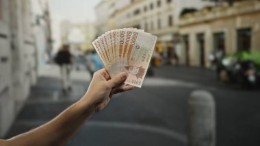 Meşgul bir şehir caddesinde Güney Kore banknotlarını elinde tutan adam, arka planda kentsel yaşamla finansal refah ve kültürel bağlam sergiliyor..