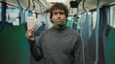 Bir otobüsün içinde elinde Czech Koruna banknotları olan İspanyol bir adam toplu taşıma araçlarında seyahat ve finans kavramlarını vurgulayan düşünceli bir ifade sergiliyor..