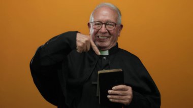 Başrahip İncil 'i tutuyor ve izole edilmiş turuncu duvarlara işaret ediyor..