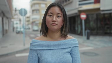 Şehir caddesinde mavi süveter giyen kadın sakin tavırları ve kapalı gözleriyle şehir mimarisi arasında gençlik huzurunu gösteriyor..