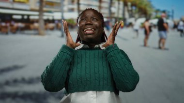 Yeşil kazaklı kadın yoğun bir sokakta duygularını ifade ediyor, şehir ve şehir manzarasıyla çevrili, dinamik açık hava enerjisi sergiliyor..