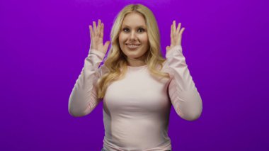 Elleri havada gülümseyen pembe gömlekli bir kadın canlı mor arka planda anlamlı, neşeli bir jest gösteriyor genç, sarışın, canlı bir kadın portresi.