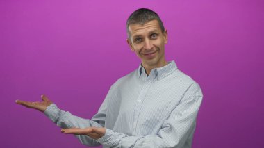 Elleri açık, parlak pembe bir arka plana karşı el kol hareketi yapan, sıradan çizgili bir gömlek giyen, kendine güvenen ve davetkar bir tavır sergileyen beyaz bir adam..