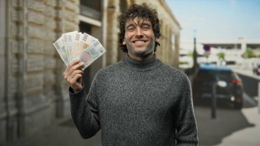 Bir şehir caddesinde elinde Czech Koruna banknotları tutan İspanyol bir adam, servetini ve başarısını şehir dışında neşeli bir ifadeyle sergiliyor..