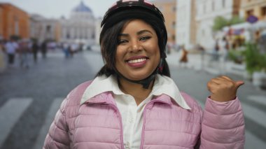 Vatikan sokak arkaplanında pembe ceketli ve miğferli gülümseyen bir kadın mutluluk ve güven saçıyor..