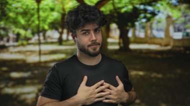 Yeşil parkta duran sakallı genç adam yazın dışarıda güneş ışığı altında duygularını ifade ediyor..