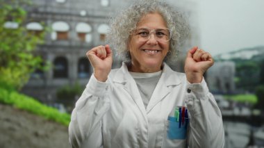 İtalya 'daki tarihi Roma stadyumunun önünde sevinçle gülümseyen laboratuvar önlüklü gri saçlı yaşlı kadın kültürel bir arka plana karşı pozitifliği ve bilimsel merakı temsil ediyor..