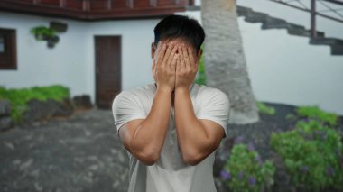 Neşeli bir ruh hali içindeki genç adam canlı bir şehir caddesinde gözlerini kapar ve yeşil bir şehir arka planında neşeli bir yüz ifadesi sergiler..