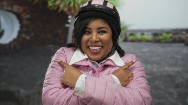 Pembe ceketli ve miğferli gülümseyen genç bir kadın şehir sokaklarında neşe ve güven gösterisi yapıyor..