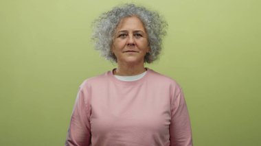 Gri saçlı yaşlı kadın sarı arka planda pembe kazak ve beyaz gömlek giyen sarı duvara karşı çılgınca bir jest yapıyor..