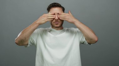 Sakallı ve gözleri açık genç bir adam izole edilmiş gri arka plana karşı şaşkınlık içinde duygularını ve merakını ifade ediyor..