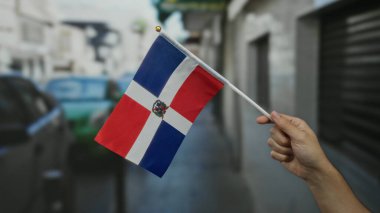 Açık şehir sokaklarında Dominik Cumhuriyeti bayrağını tutan adam beyaz eliyle kültürel gurur ve vatanseverlik sergiliyor..