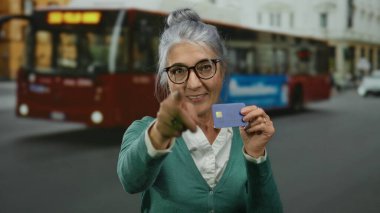 Yoğun caddede elinde kredi kartıyla gülümseyen bir kadın, arka planda otobüsle, şehir yaşam tarzını ve finansal bağımsızlığı vurguluyor.