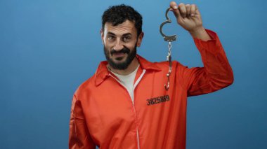 Turuncu hapishane tulumlu, mavi arka planda kelepçeli İspanyol sakallı adam tutukluluk temasını betimliyor..