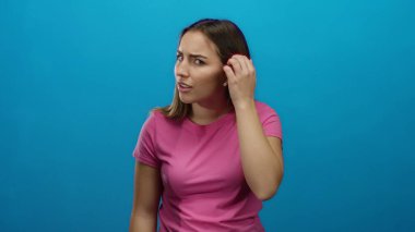 Pembe gömlekli kadın, mavi arkaplan karşısında el pençe divan durup, izole stüdyo ortamını merak ve ilgi gösteriyor..