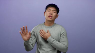 Gri kazaklı genç Çinli adam dürüstlük ve güveni ifade eden mor arka plan duvarının üzerinden el pençe divan durarak samimi jestler yapar..