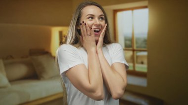 Beyaz tişörtlü, uzun saçlı genç bir kadın pencereden içeri güneş ışığı süzülen sıcak bir odada şaşkın ve mutlu hissediyordu..