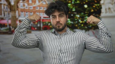 Latin kökenli genç bir adam şehrin önünde esniyor sakallı ve çizgili gömlekli özgüvenini gösteriyor.