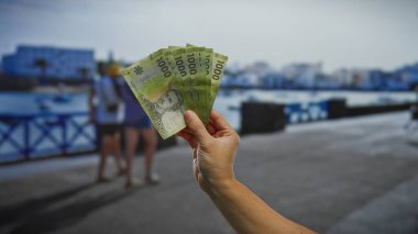 Şili pesolarını sahil limanına yakın bir yerde tutan bir adamın eli, canlı bir kasaba ortamında açık hava tatili harcamalarının özünü yakalıyor..