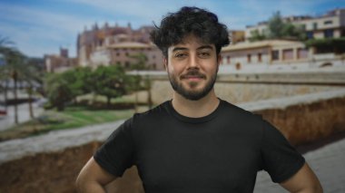 Güneşli bir günde, güzel bir mimari ve yemyeşil ile çevrili, canlı bir atmosferi olan tarihi bir Akdeniz şehrinde, açık havada gülümseyen genç sakallı adam..