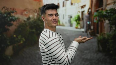 Çizgili süveter giyen genç bir adam çekici bir şehir caddesinde hareketli bir yeşillikle açık hava ortamında kendinden emin ve çekici bir hava yayıyor..