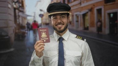 Pilot üniformalı genç bir adam Filipinli bir pasaport tutuyor, canlı bir sokakta açık havada gülümsüyor, seyahat ve havacılık temalarını sergiliyor..