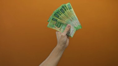 İzole edilmiş turuncu bir arkaplan üzerinde Rus rublesi tutan beyaz bir adamın eli, banknotların canlı bir şekilde sergilendiği finansal kavramları resmediyor..