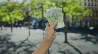 Güneşli bir şehir sokağında arka planda ağaçlar olan Singapur dolarları tutan adam.