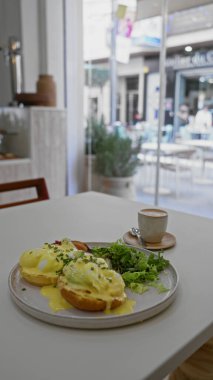 Lezzetli yumurtalı Benedict, modern dekorlu rahat bir restoranın masasında taze ve davetkar bir ortam sunuyor. Brunch meraklıları ve yemek sevenler için mükemmel..