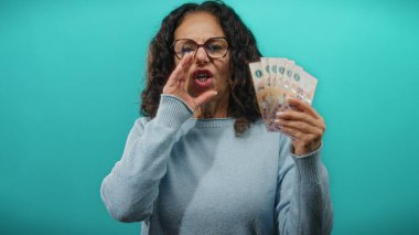 Arjantinli pezolarla gülümseyen ve bağıran bir kadın izole edilmiş mavi bir duvarın üzerinde bir anlık heyecan ve finansal refah yakalıyor..