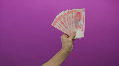 Kafkas adam Endonezya para biriminin birden fazla pembe banknotlarını canlı pembe izole bir zemin üzerinde tutuyor, finansal kavramları ve canlı renk karşıtlığını vurguluyor..