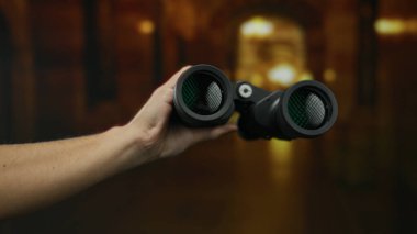 Gizemli üniversite koridoru arka planında dürbünü tutan adam akademik bir ortamda keşif ve merak duygusunu vurguluyor..