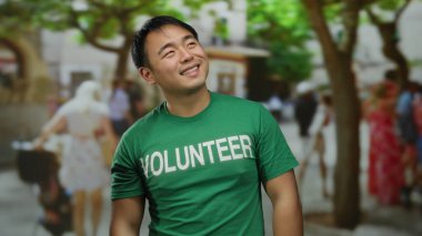 Yoğun şehir sokaklarında insanların ve ağaçların bulanık geçmişine sahip, gönüllü gömlekli genç adam gülümsüyor..