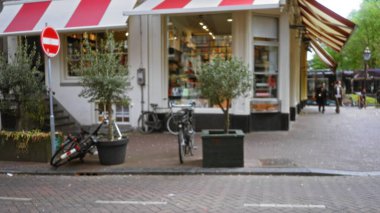 Bisikletli bir Avrupa caddesinin bulanık görüntüsü, fırının önünden geçen erkek ve kadın büyüleyici, açık hava ortamında kırmızı bir tentenin altında yürüyorlar..