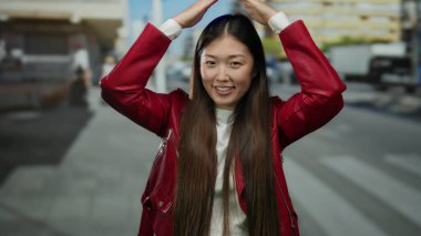 Kırmızı ceketli bir kadın, bir şehir caddesinde neşeli bir şekilde gülümsüyor ve poz veriyor, şehir modasını ve canlı bir açık hava havasını sergiliyor..