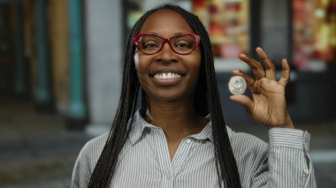 Şehir merkezinde elinde ethereum para tutan kadın şifreli para sergiliyor. Kendine güveni tam, örgülü saç stili, gözlük ve çizgili gömlek takıyor..