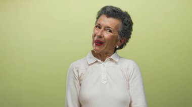 Sarı arka planda, gri saçlı yaşlı kadın şakacı ve esprili tavırlar sergiliyor..