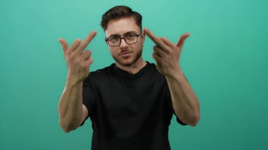 Sakallı genç adam, siyah gömlek ve gözlük takarak yeşil arka planda duran orta parmaklarıyla saldırgan hareketler yapıyor.