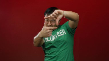 Genç adam, elleri kırmızı arka planda, yeşil gömlekli, dostça bir ifade sergileyen, çerçeveli jestler yapıyor..