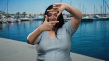 Kadın arka planda teknelerle deniz kenarında neşeli bir şekilde poz veriyor, neşeli, açık hava atmosferini somutlaştırıyor.