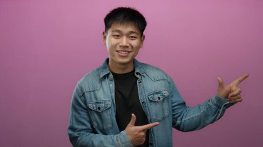 İzole edilmiş pembe arka planda ifade ile parlayan genç bir adam kot ceket giyiyor, oyunculuk ve enerji gösteriyor.
